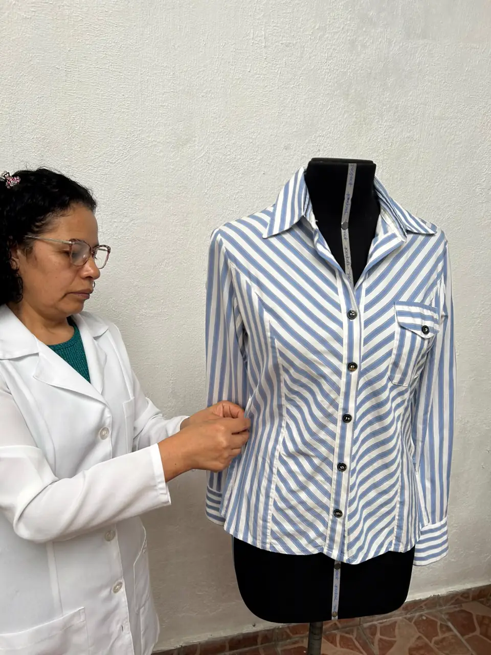 Costureira ajustando a lateral de uma camisa listrada azul e branca no manequim