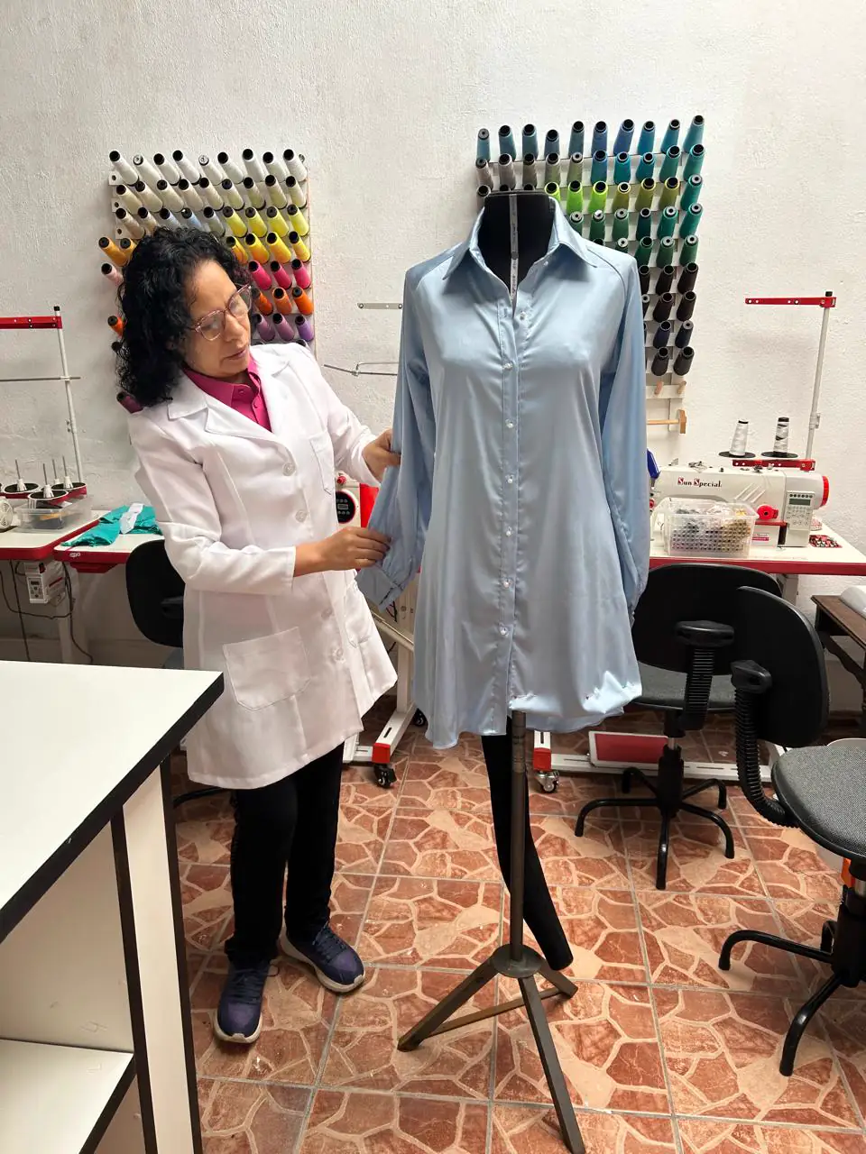 Costureira do ateliê ajustando a manga de uma camisa azul-clara no manequim