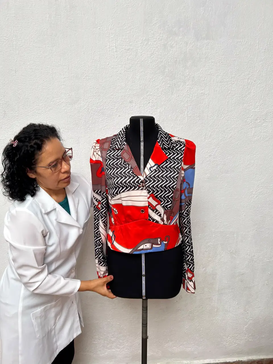 Costureira conferindo o caimento de uma jaqueta estampada vermelha, preta e branca no manequim