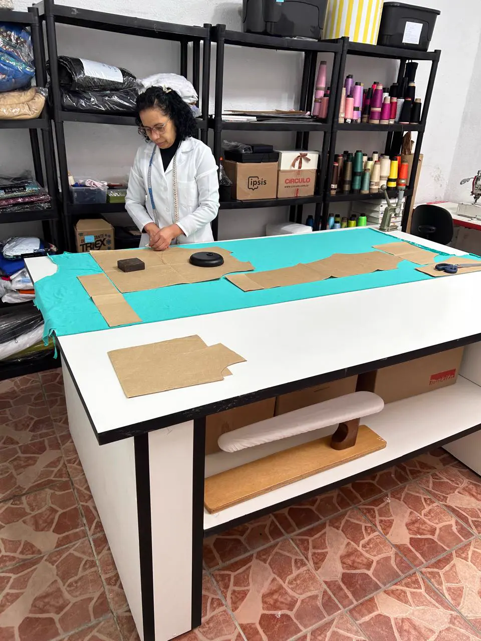 Costureira de jaleco branco trabalhando na mesa de corte do ateliê